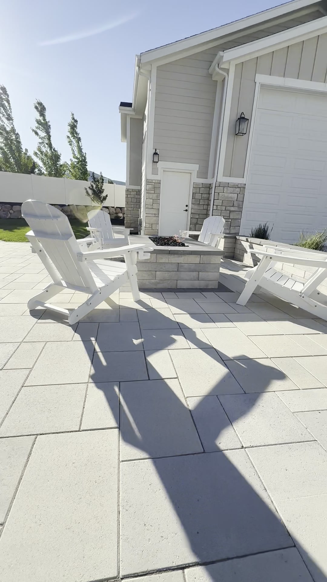Adirondack chairs around a fire pit on a tumbled paver patio with stone-faced home behind